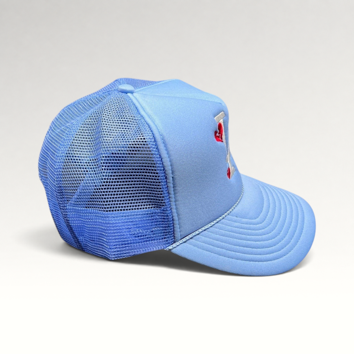 Raree Finds light-blue Y2K trucker hat with white LA logo and red broken-heart embroidery on a foam front mesh cap.