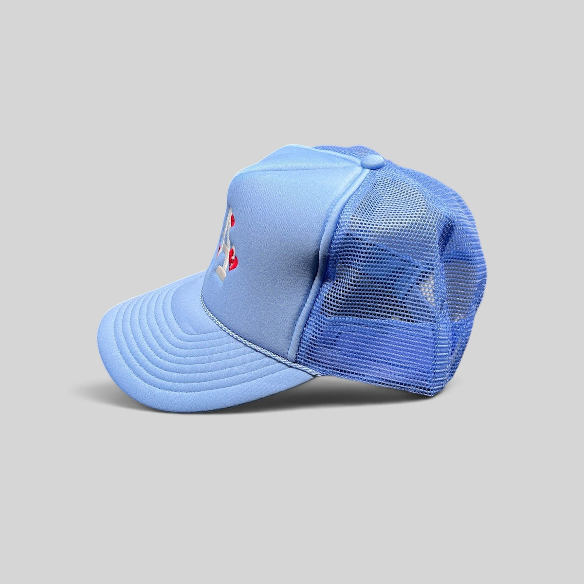 Raree Finds light-blue Y2K trucker hat with white LA logo and red heart embroidery, featuring a mesh back and snapback.