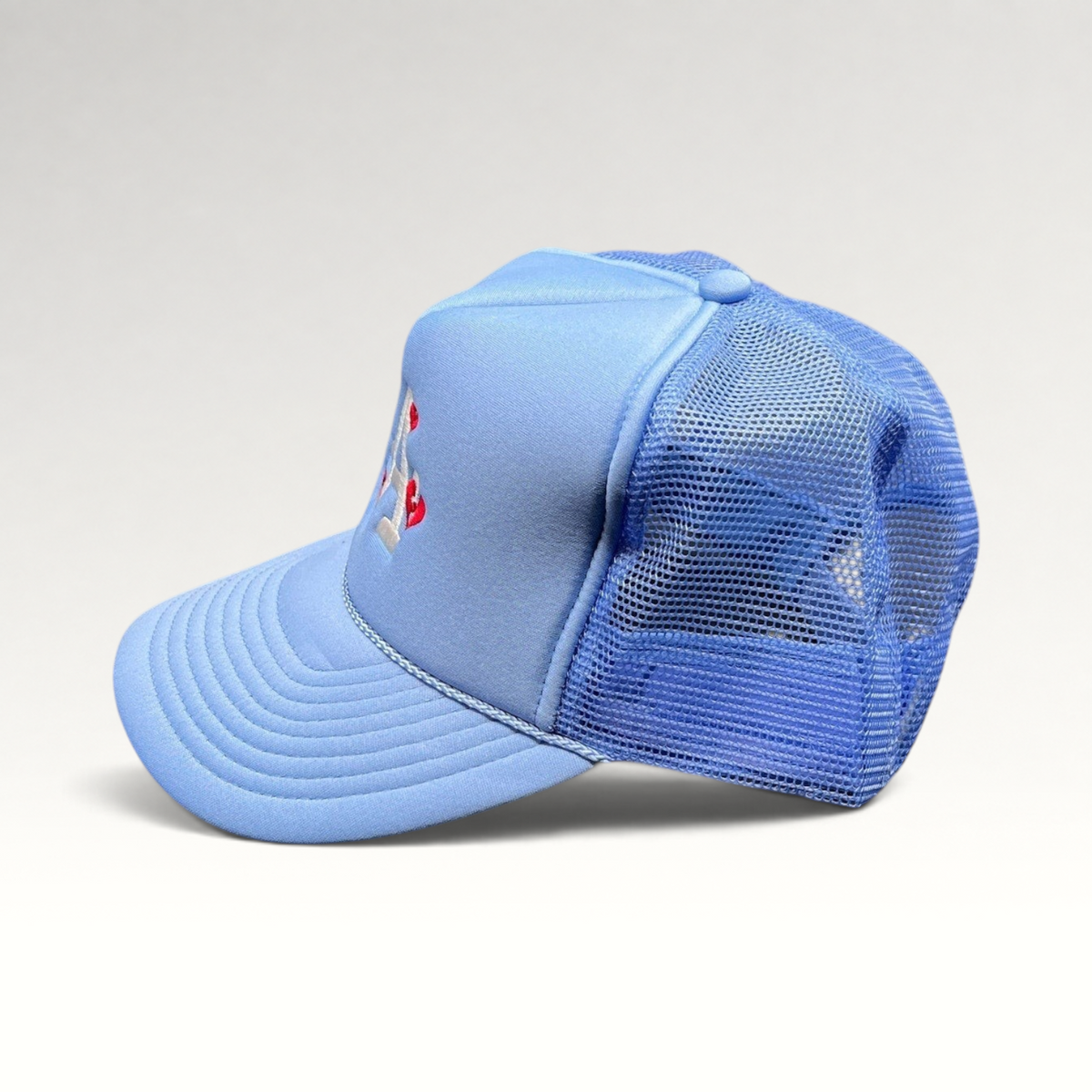 Raree Finds light-blue Y2K trucker hat with white LA logo and red heart embroidery, featuring a mesh back and snapback.