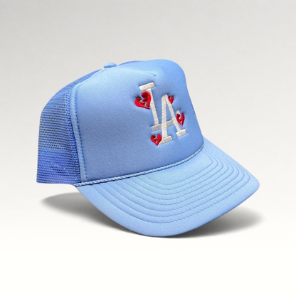 Raree Finds light-blue Y2K trucker hat with white LA logo and red broken-heart embroidery on a foam-front mesh cap.