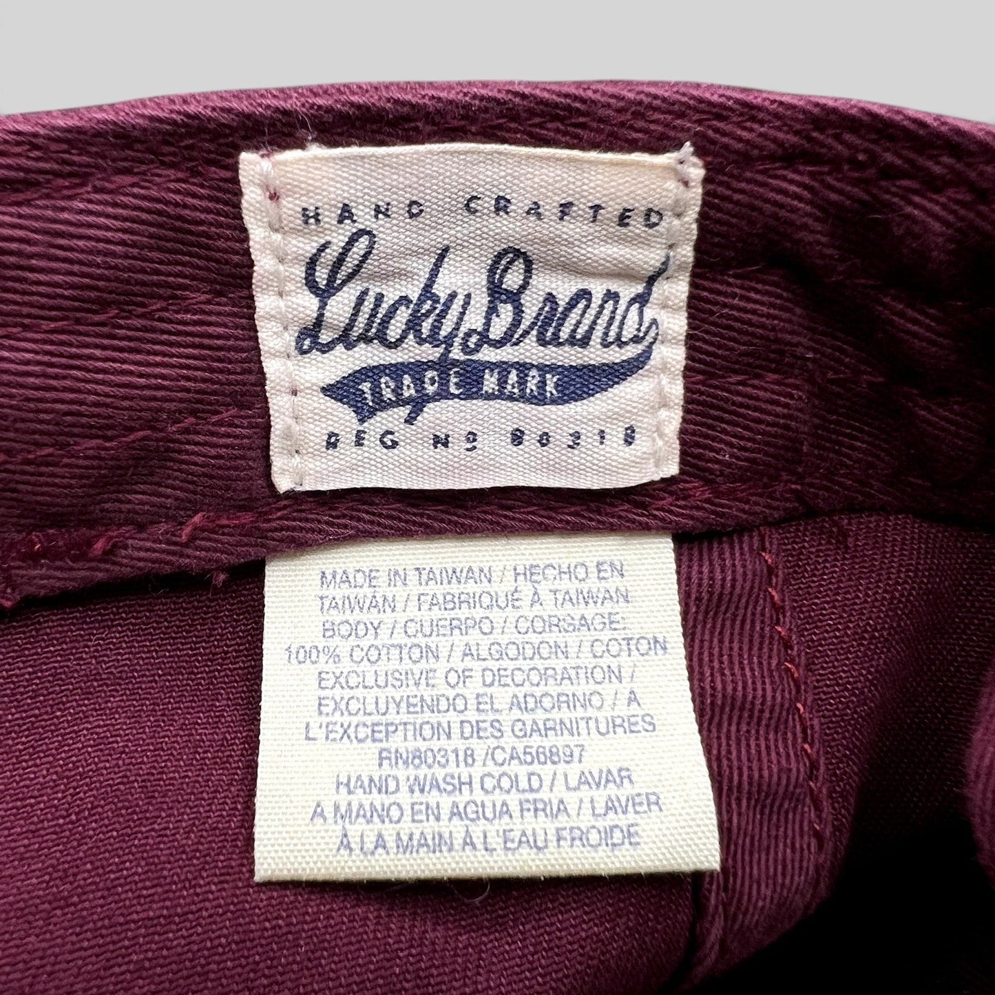Raree Finds Lucky Brand x Budweiser hat interior label showing cotton material and care instructions in burgundy