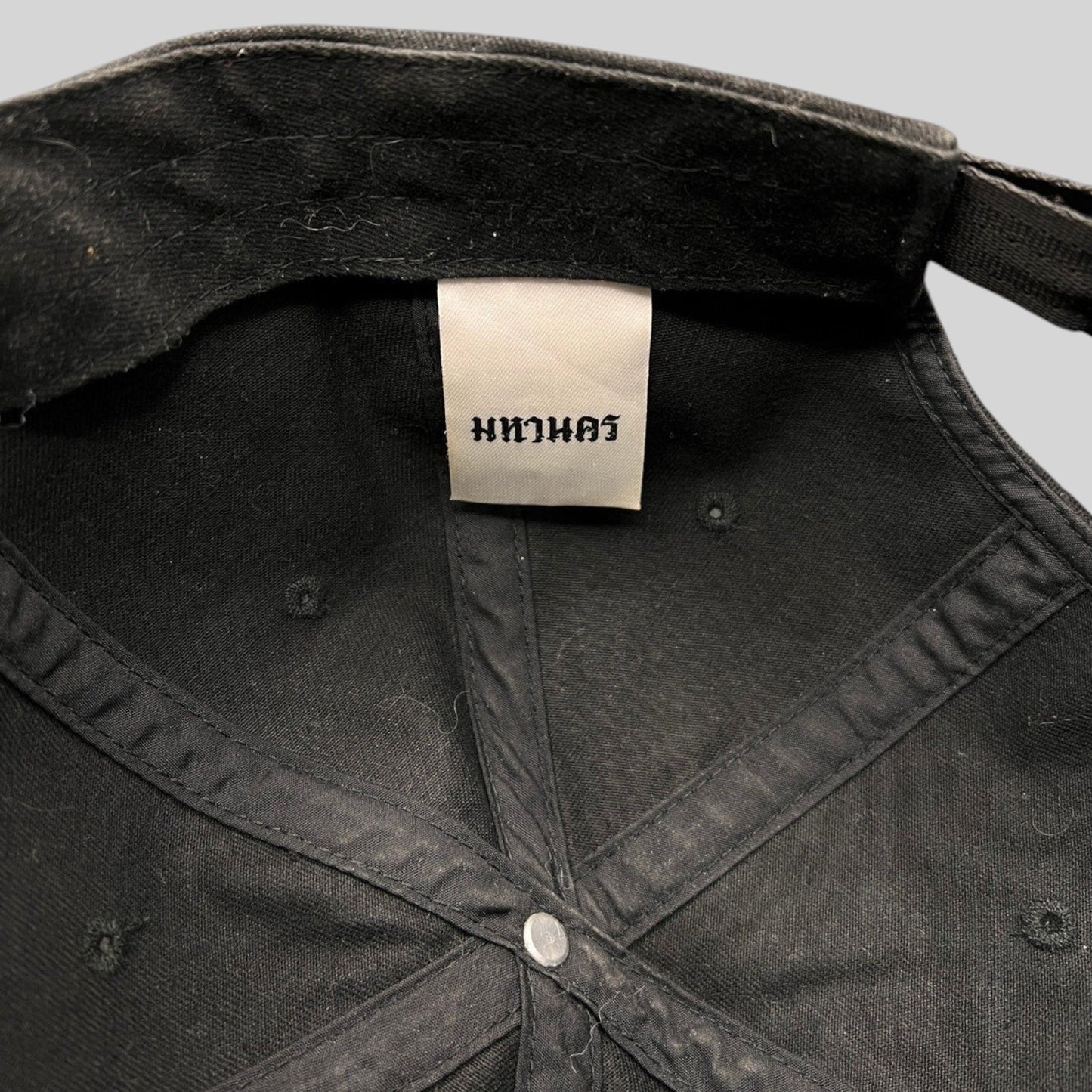 Interior view of a black Raree Finds Mahanakhon cotton strapback hat showing the authentic woven brand tag