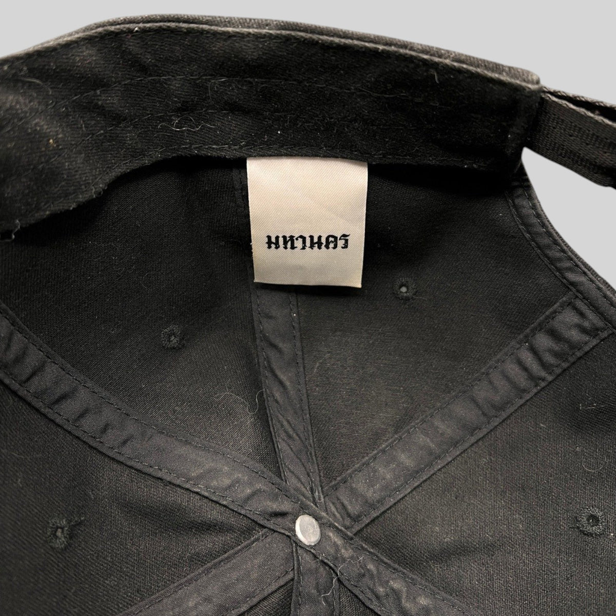 Interior view of a black Raree Finds Mahanakhon cotton strapback hat showing the authentic woven brand tag
