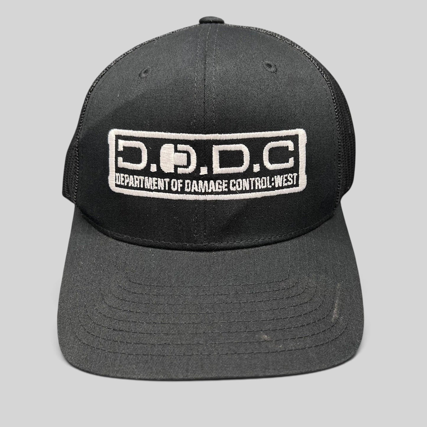 Raree Finds black Marvel Damage Control trucker hat with D.O.D.C. West embroidered patch and mesh back panels.