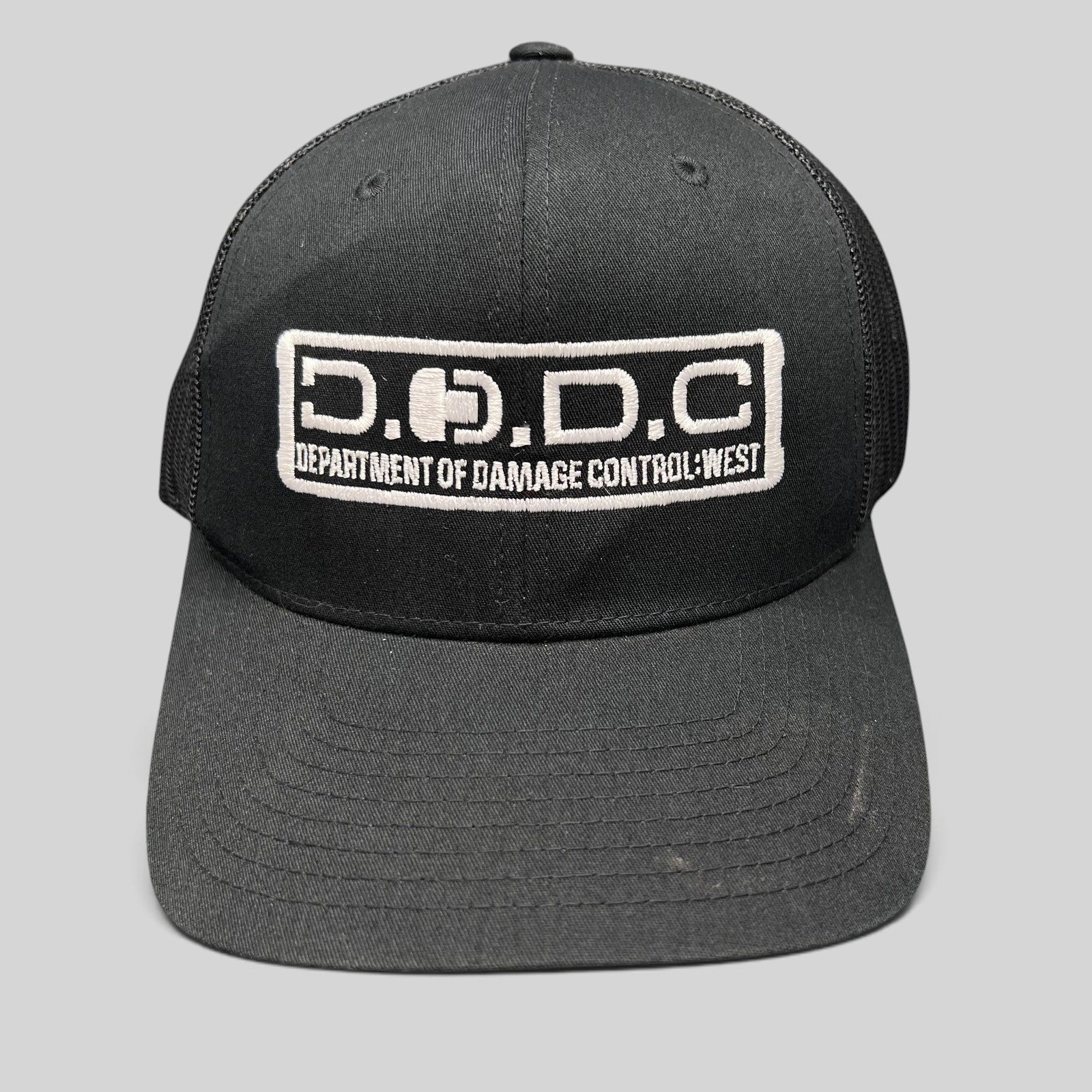 Raree Finds black Marvel Damage Control trucker hat with D.O.D.C. West embroidered patch and mesh back panels.