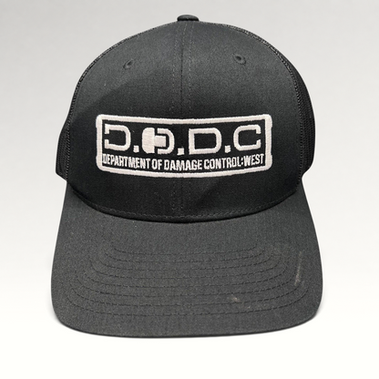 Raree Finds black Marvel Damage Control trucker hat with D.O.D.C. West embroidered patch and mesh back panels.