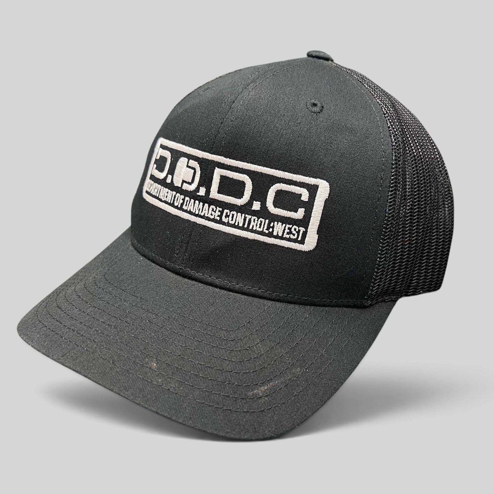 Raree Finds black Marvel Damage Control D.O.D.C. West trucker hat with mesh back and adjustable snapback closure.