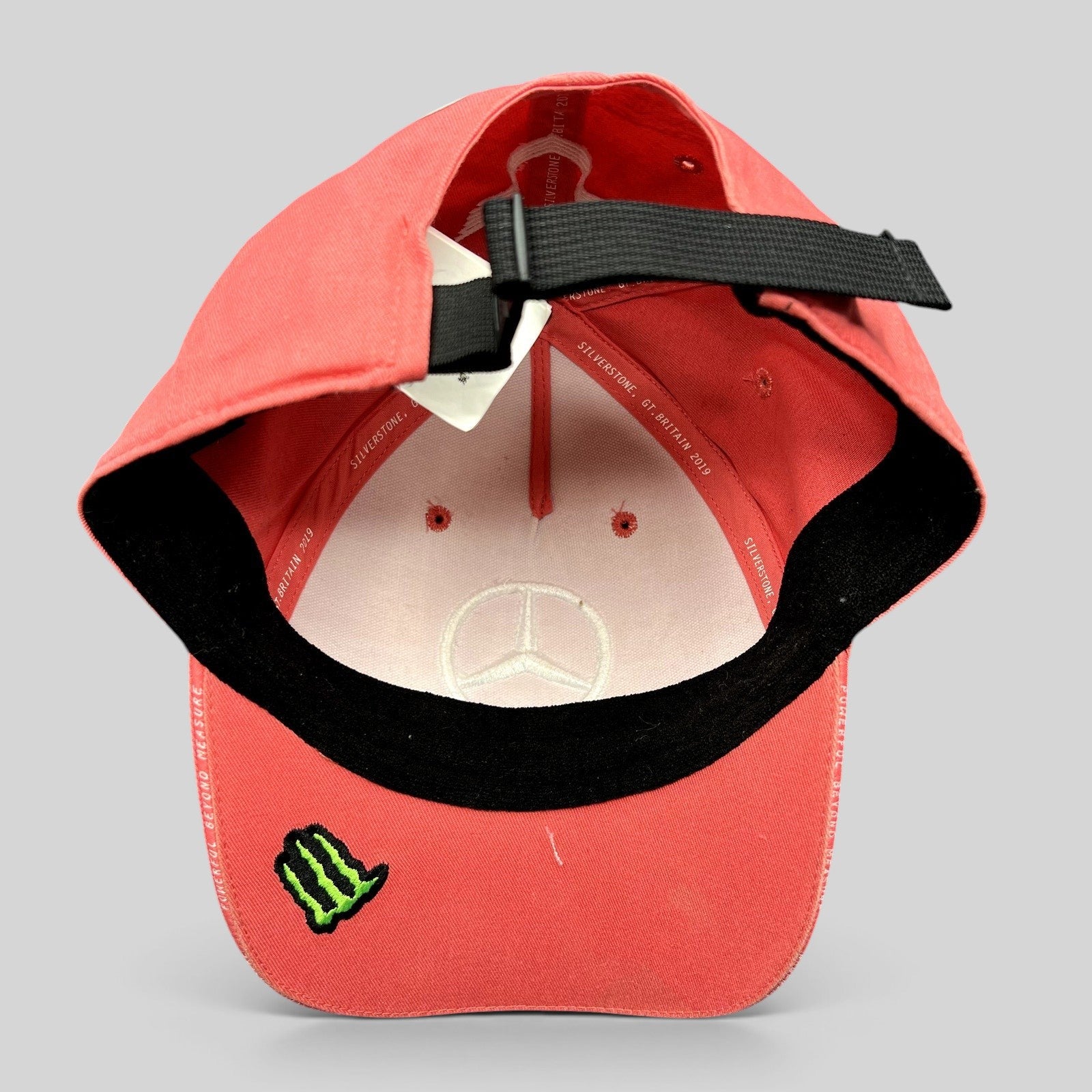 Raree Finds Mercedes AMG Petronas strapback hat in coral pink with Monster Energy logo under the brim and black strap.