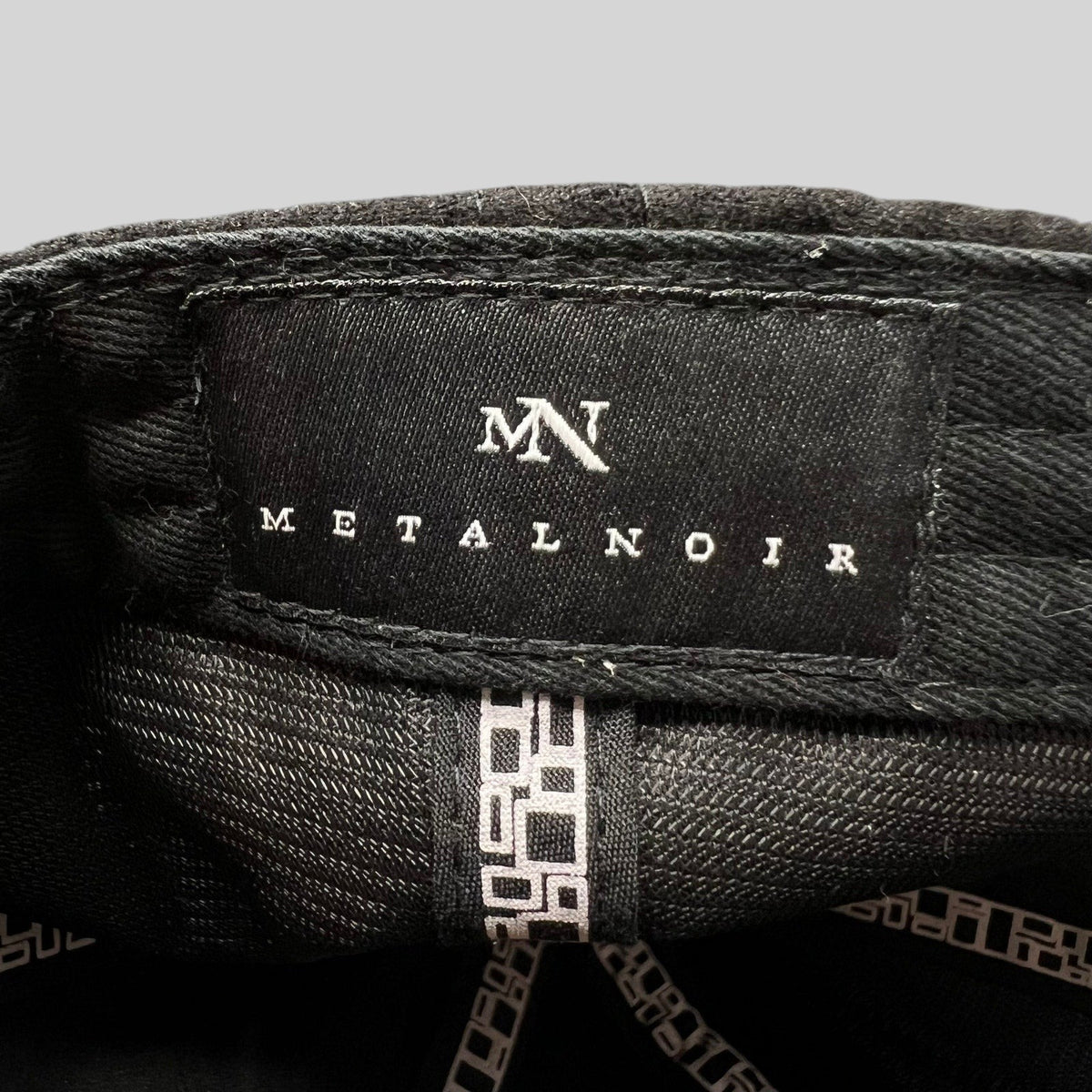 Raree Finds Metal Noir black strapback hat interior label with white MN logo and brand name on black fabric