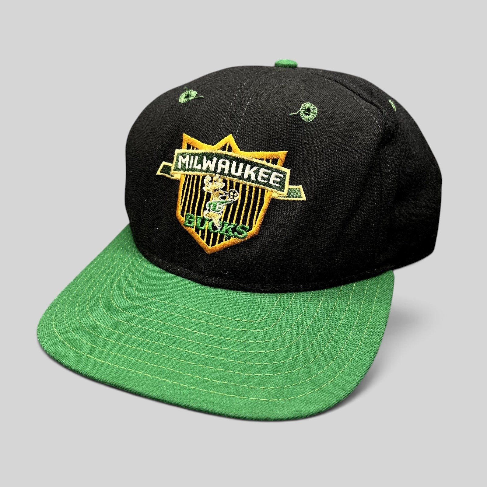 Raree Finds vintage Milwaukee Bucks New Era snapback hat with black crown, green brim, and embroidered shield logo.