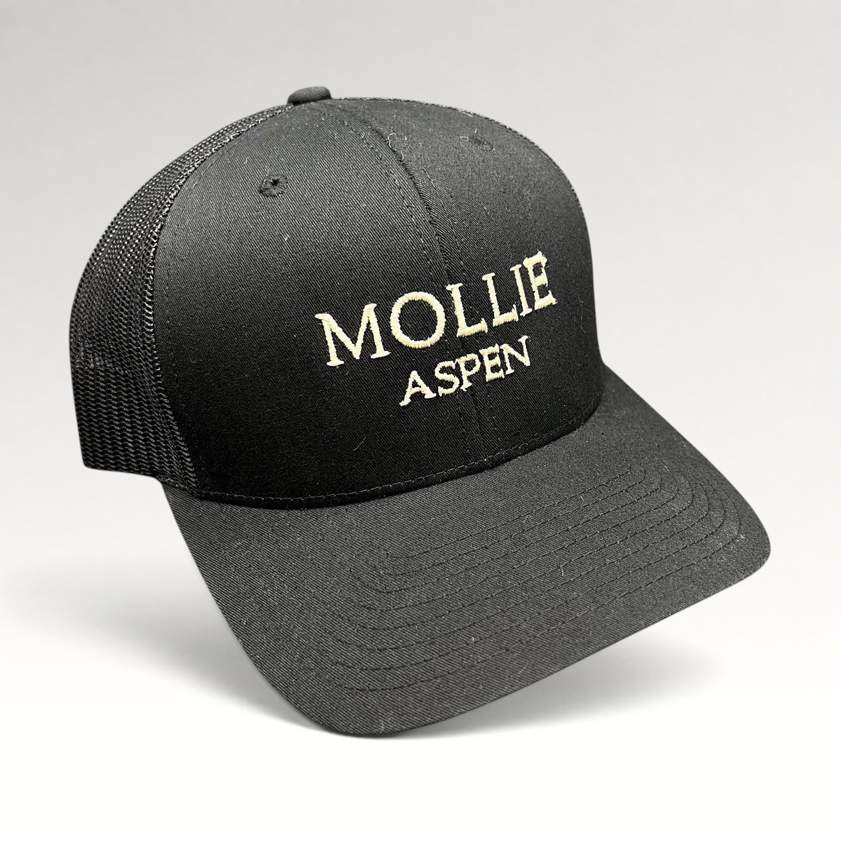 Raree Finds black MOLLIE Aspen trucker hat with embroidered logo, structured front, and breathable mesh back panels.
