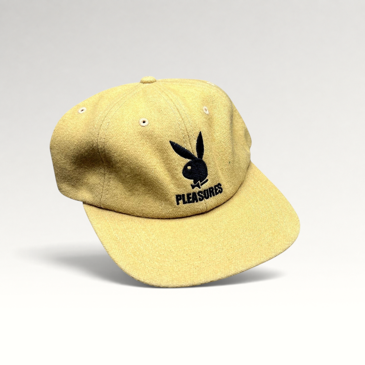 Raree Finds mustard Melton wool strapback hat featuring an embroidered black Playboy Bunny and PLEASURES logo.