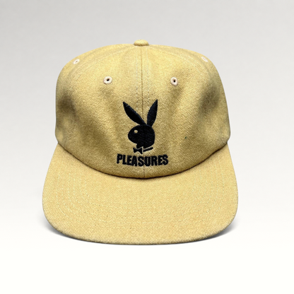 Raree Finds mustard wool strapback hat featuring an embroidered black Playboy Bunny and PLEASURES logo on the front.