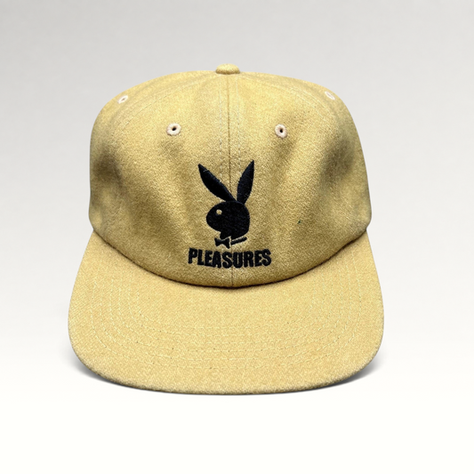 Raree Finds mustard wool strapback hat featuring an embroidered black Playboy Bunny and PLEASURES logo on the front.