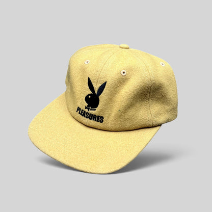 Raree Finds mustard wool strapback hat featuring an embroidered black Playboy Bunny and PLEASURES logo on the front