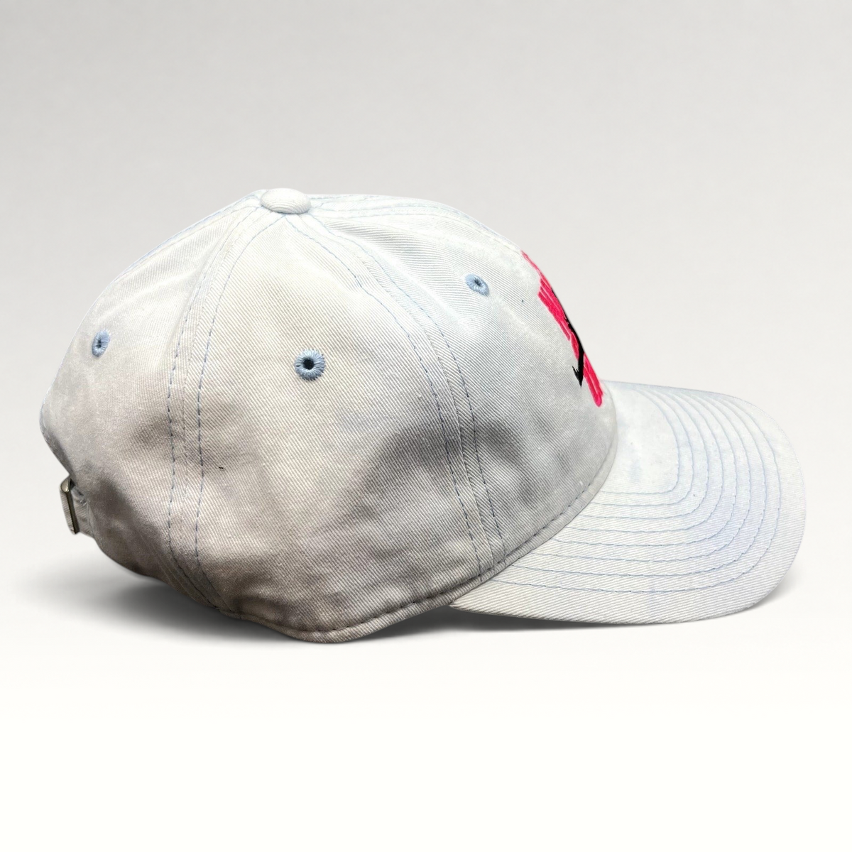 Raree Finds white cotton strapback hat with pink The Naked Gun embroidery and light blue stitching, side view.