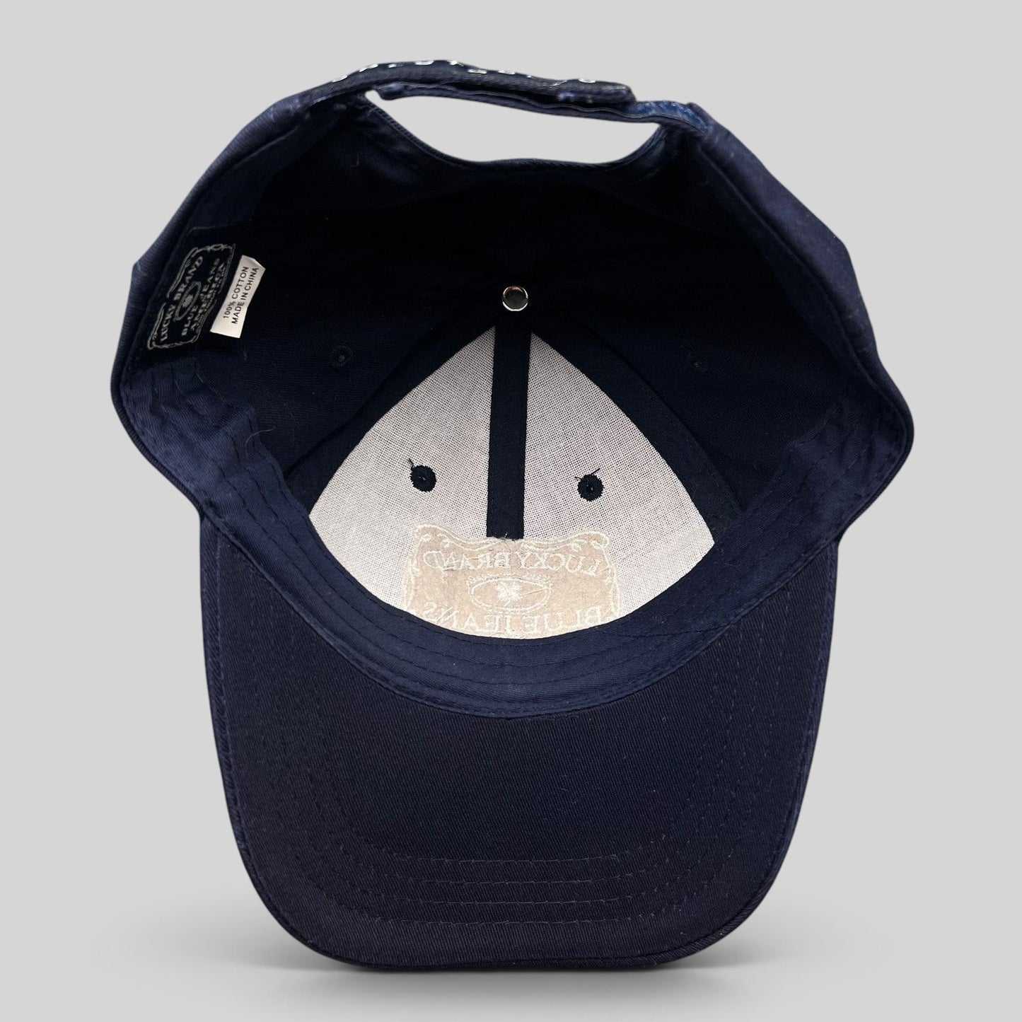 Raree Finds navy cotton snapback cap interior showing Lucky Brand label and white embroidered logo on the brim
