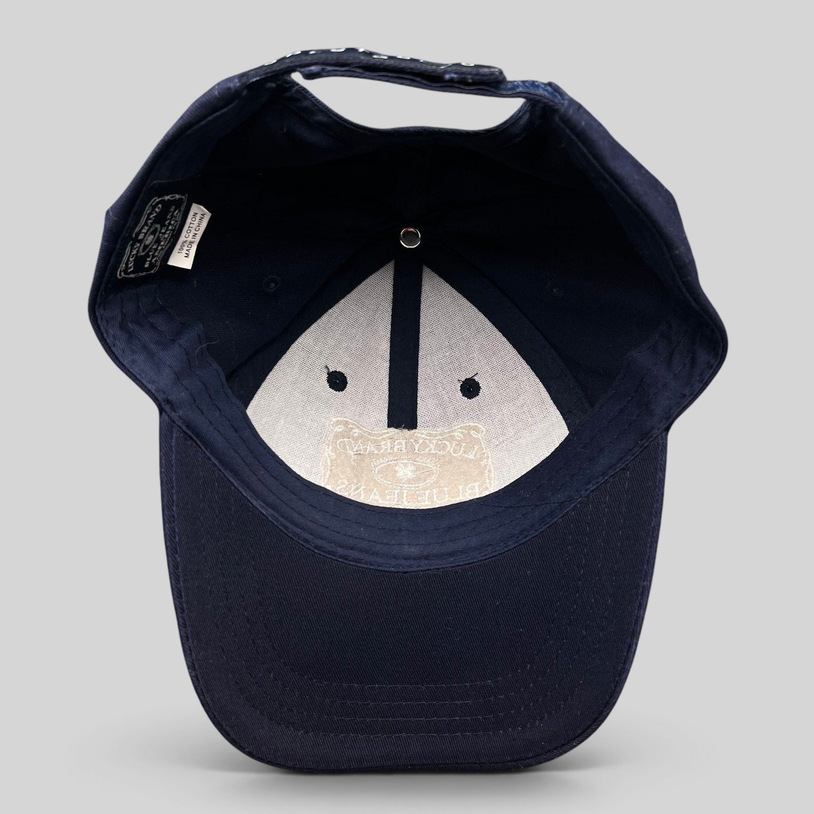 Raree Finds navy cotton snapback cap interior showing Lucky Brand label and white embroidered logo on the brim