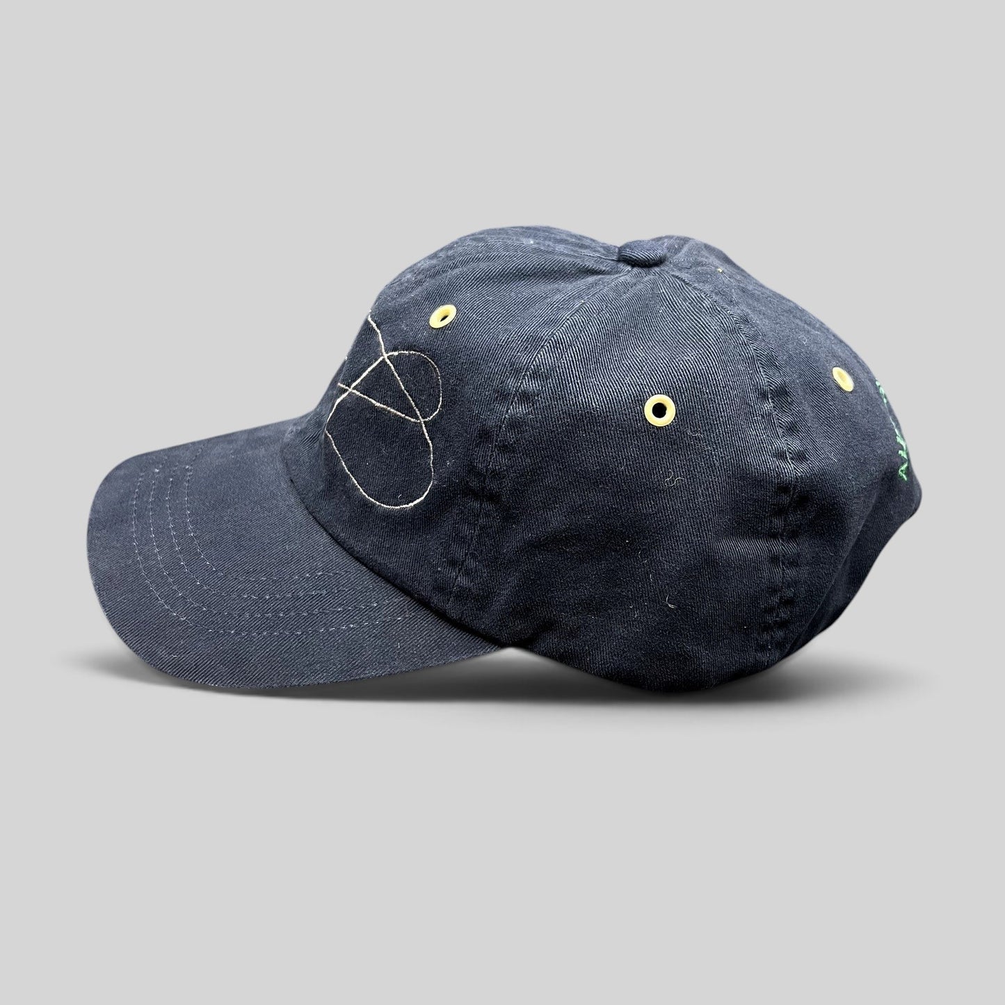 Raree Finds navy cotton strapback hat with embroidered fly fishing design and yellow metal eyelets, side view.