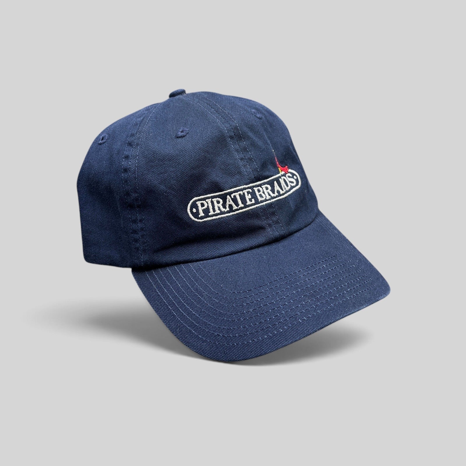 Raree Finds navy cotton dad hat with embroidered Pirate Brands logo and red parrot detail on a curved brim cap.