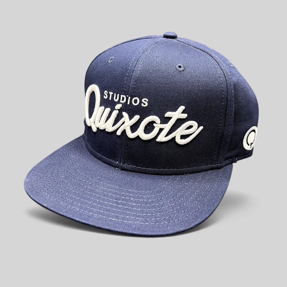 Raree Finds navy blue snapback hat with white raised Quixote Studios embroidery and flat brim