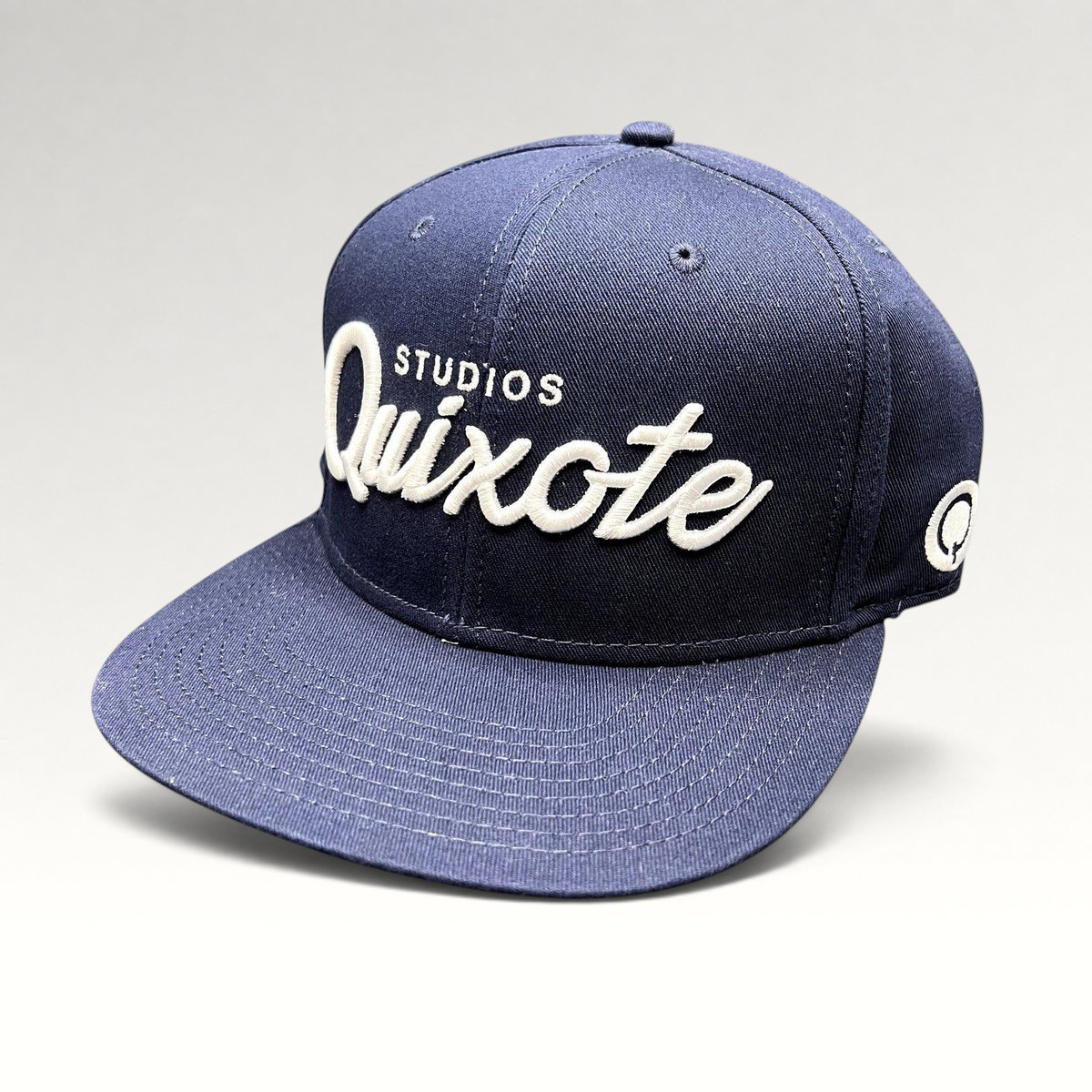 Raree Finds navy blue snapback hat with white raised Quixote Studios embroidery and flat brim