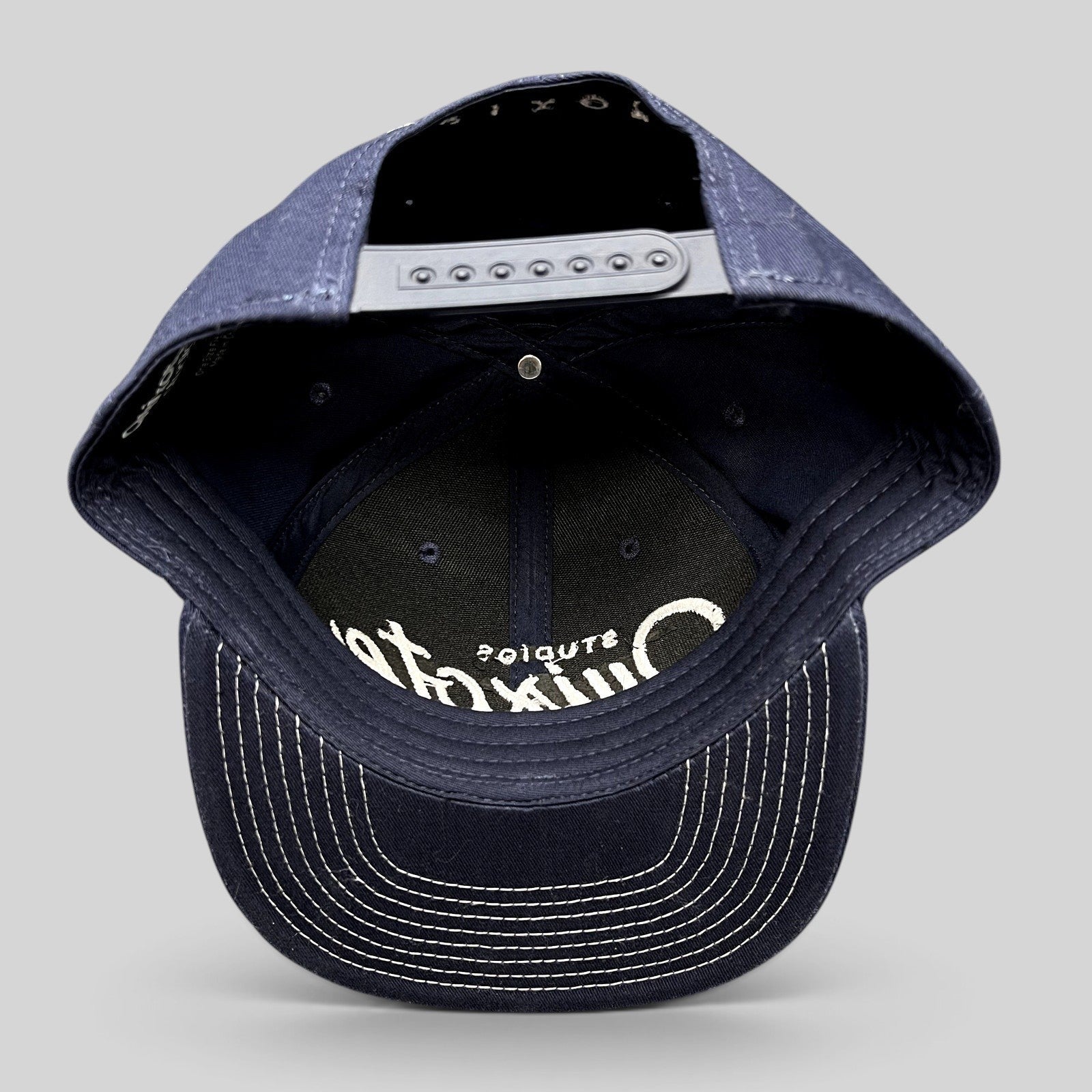 Raree Finds navy blue Quixote Studios snapback hat with white embroidered logo and adjustable plastic back closure
