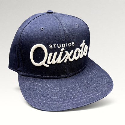 Raree Finds navy blue snapback hat with raised white Quixote Studios embroidery on the structured crown and flat brim.