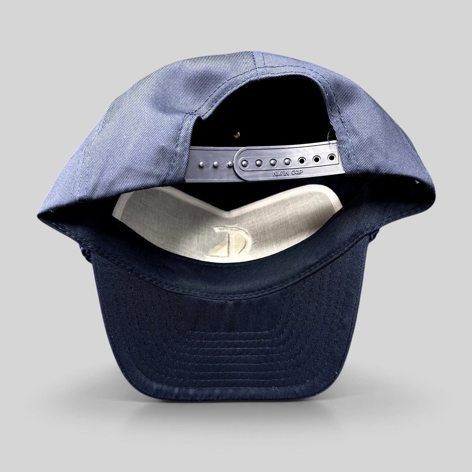 Raree Finds navy blue Nissin Cap snapback hat showing the adjustable plastic strap and interior white lining
