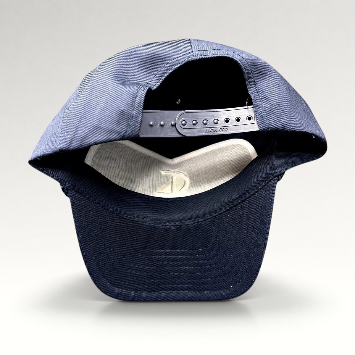 Raree Finds navy blue Nissin Cap snapback hat showing the adjustable plastic strap and interior white lining