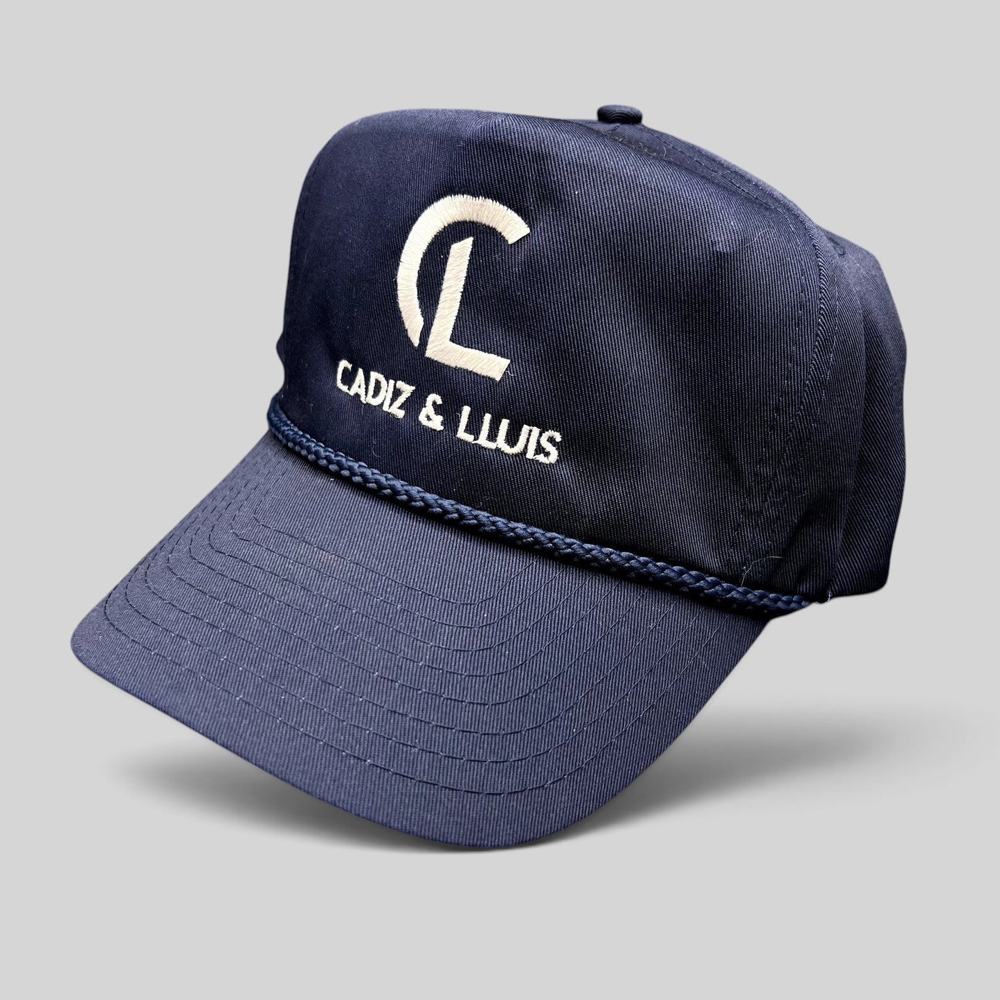 Raree Finds navy blue vintage snapback hat with white Cadiz & Lluis embroidered logo and braided rope bill detail.