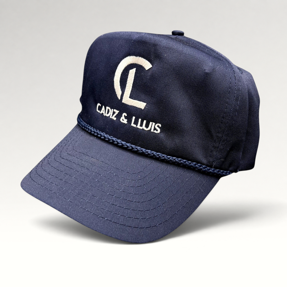 Raree Finds navy blue vintage snapback hat with white Cadiz & Lluis embroidered logo and braided rope bill detail.