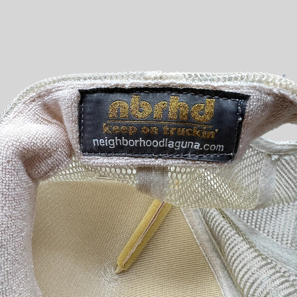 Raree Finds NBRHD Neighborhood Laguna trucker hat interior label with gold glitter branding on cream mesh fabric