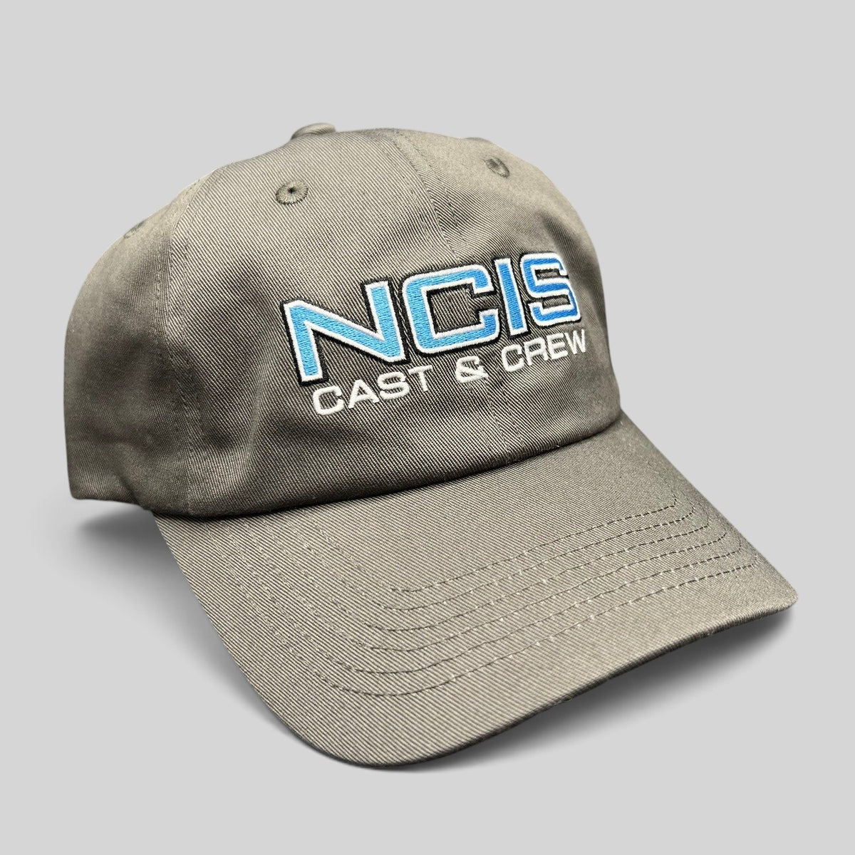 Raree Finds gray NCIS Cast & Crew strapback hat with blue and white embroidered logo on a curved bill cap.