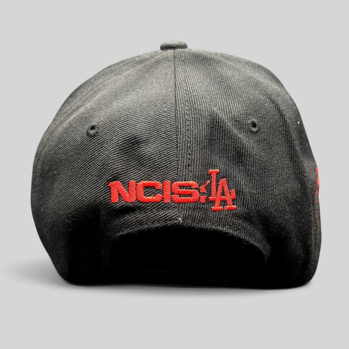 Raree Finds black snapback hat featuring red NCIS LA embroidery on the back, commemorative television show merchandise.