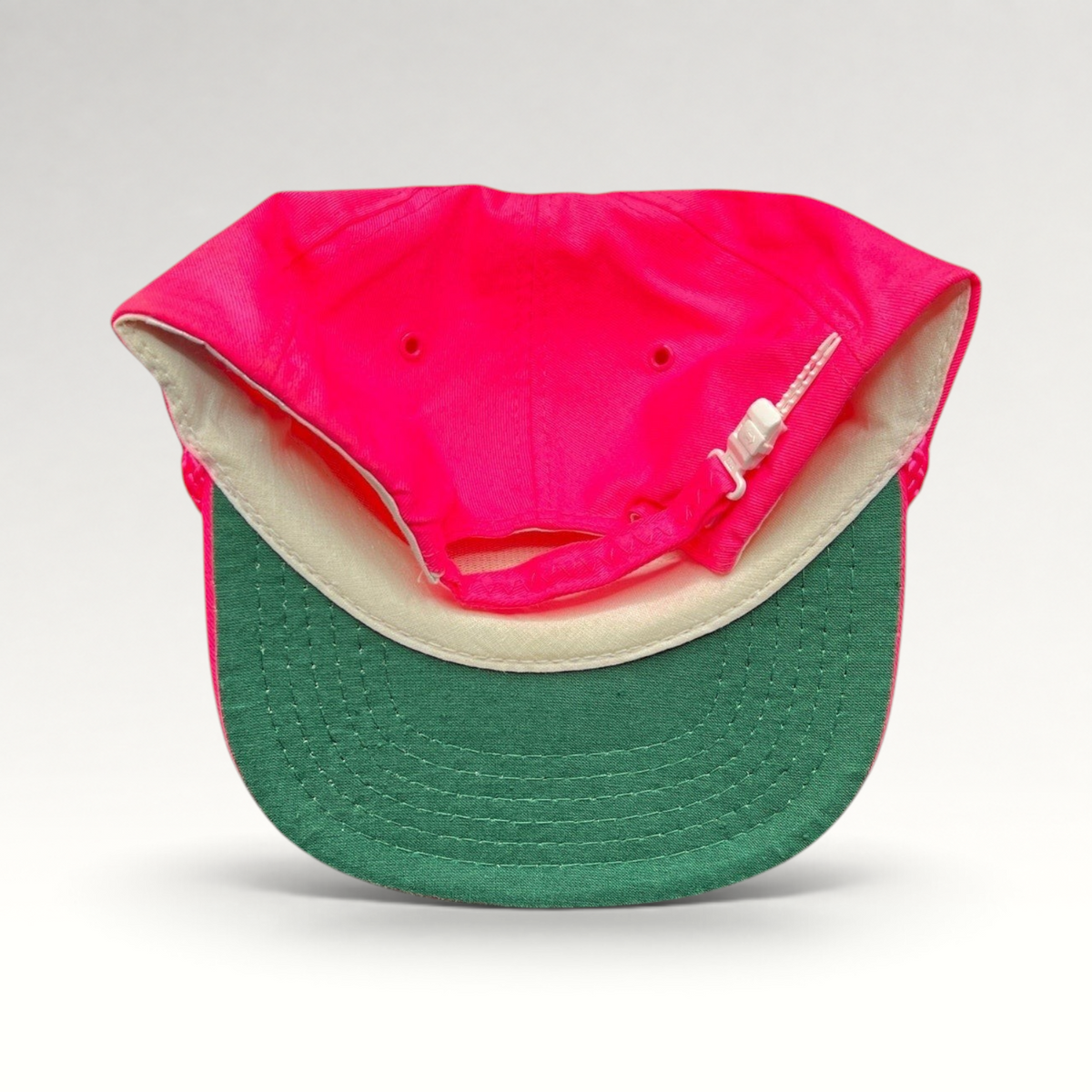 Raree Finds vintage 1980s neon pink snapback hat with a green undervisor and white plastic zipperback closure.