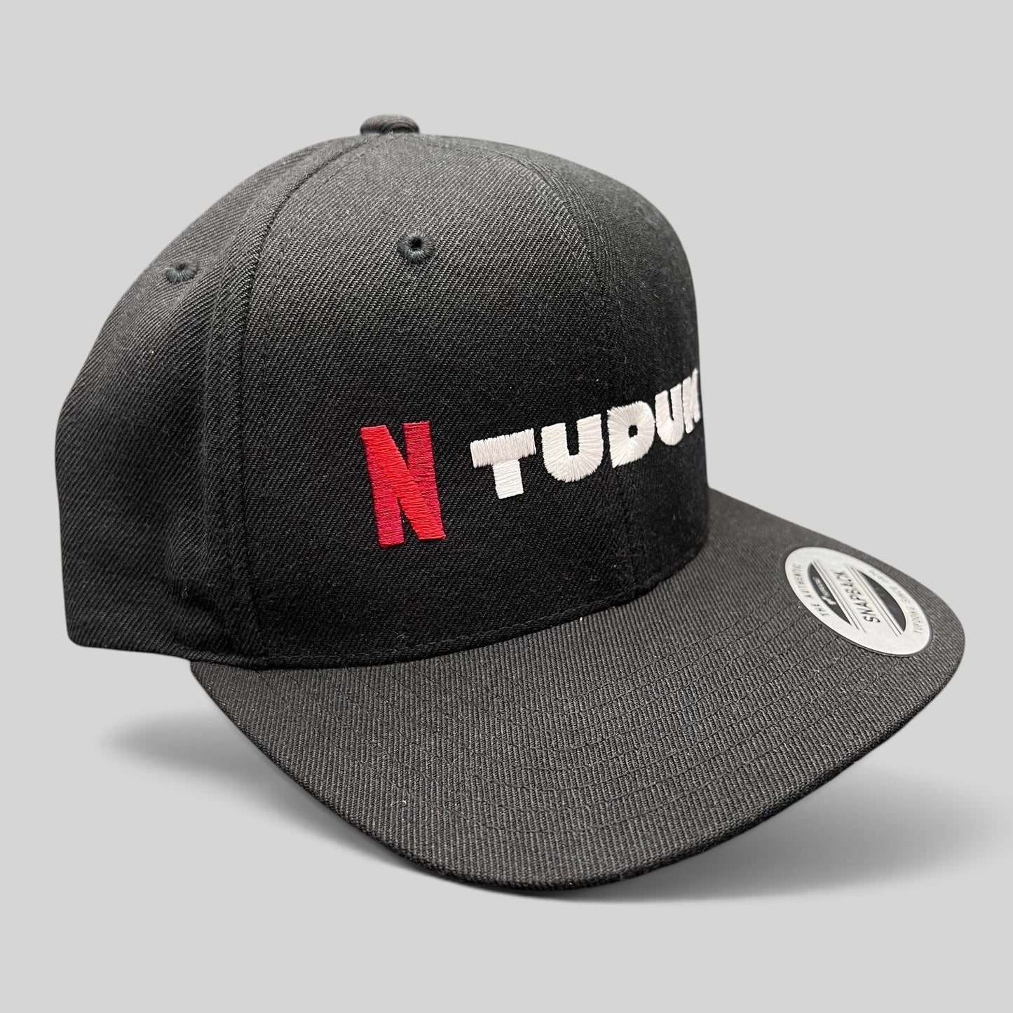 Raree Finds Netflix Tudum black snapback hat with red N logo and white TUDUM embroidery on a Yupoong classic cap.