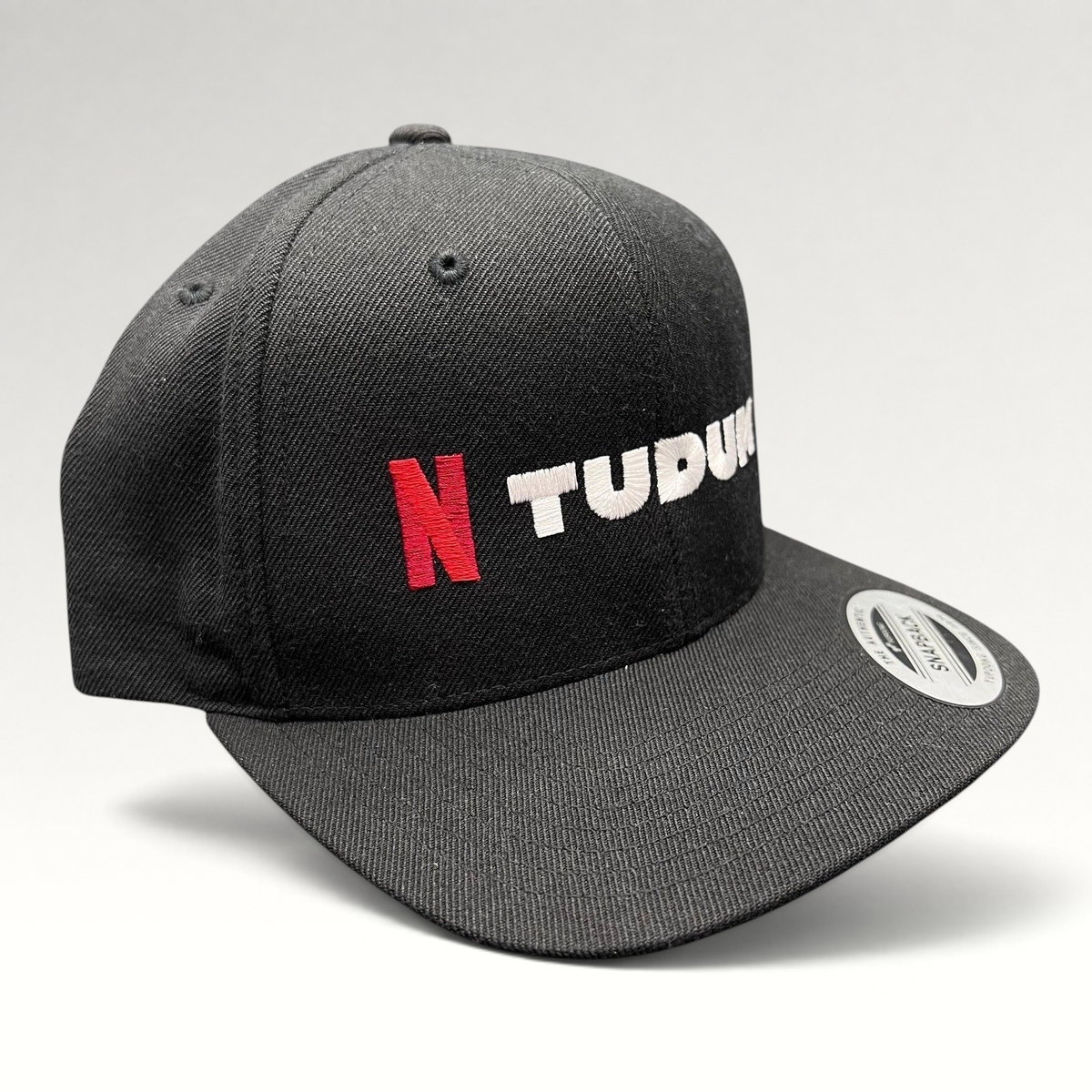Raree Finds Netflix Tudum black snapback hat with red N logo and white TUDUM embroidery on a Yupoong classic cap.