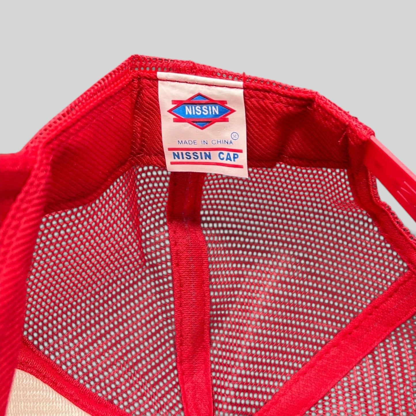 Raree Finds Nissin Cap red trucker hat interior label showing brand logo and mesh construction details