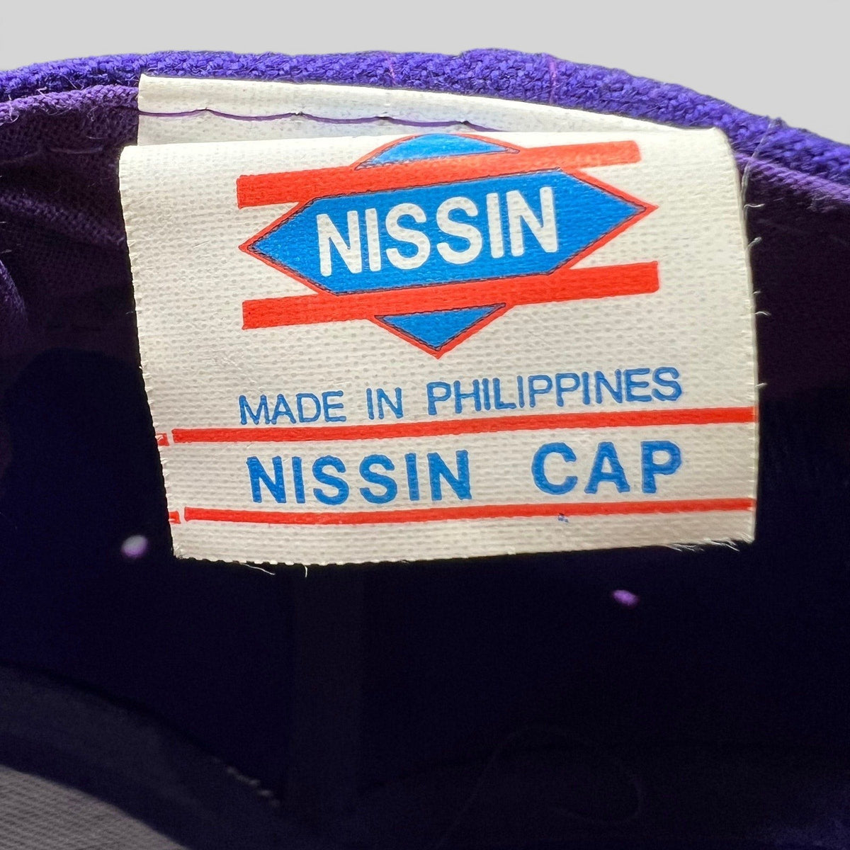 Raree Finds vintage 90s Nissin cap interior label showing brand logo and Made in Philippines text on purple fabric