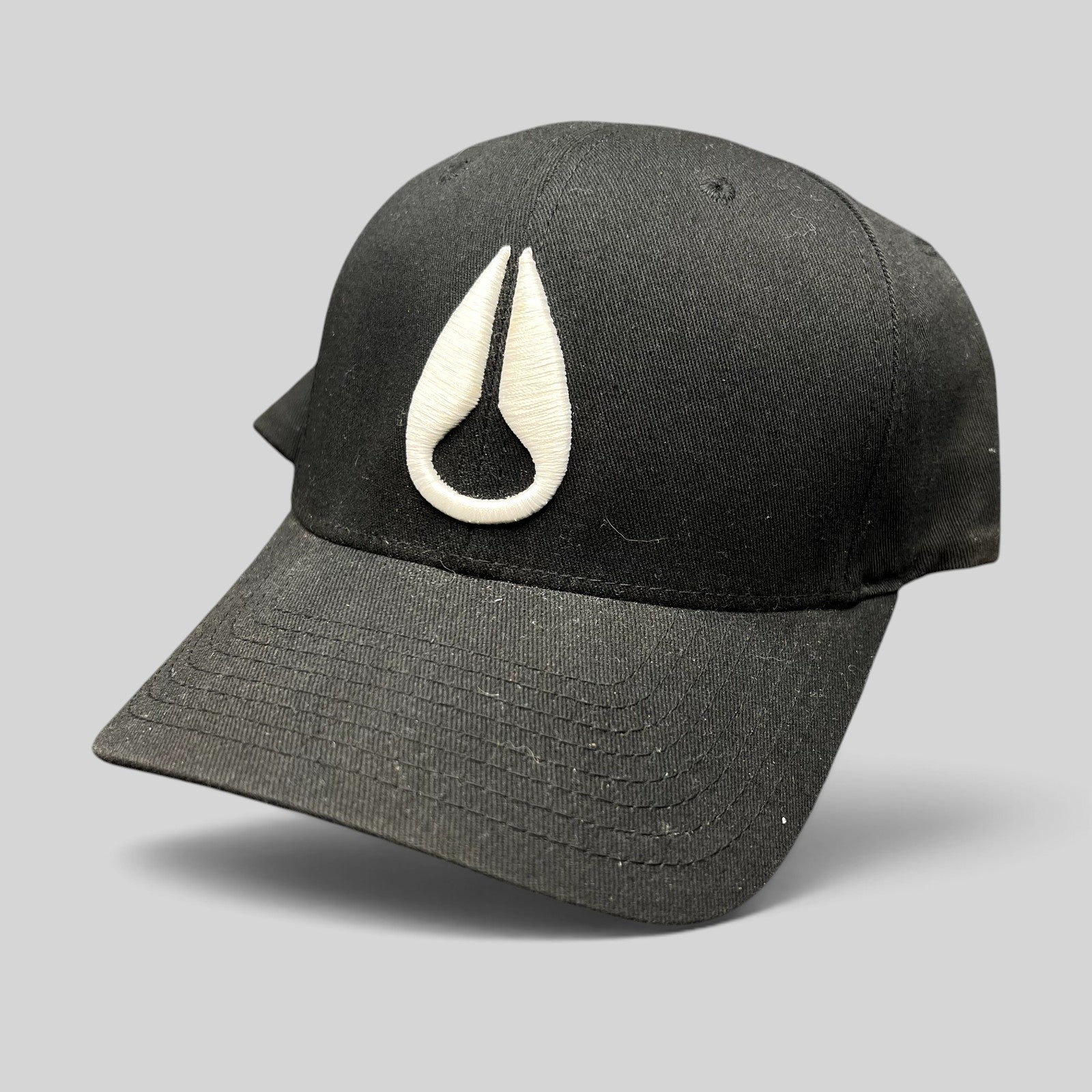 Raree Finds black Flexfit cap with white embroidered Nixon droplet logo, featuring a stretch-fit cotton construction.