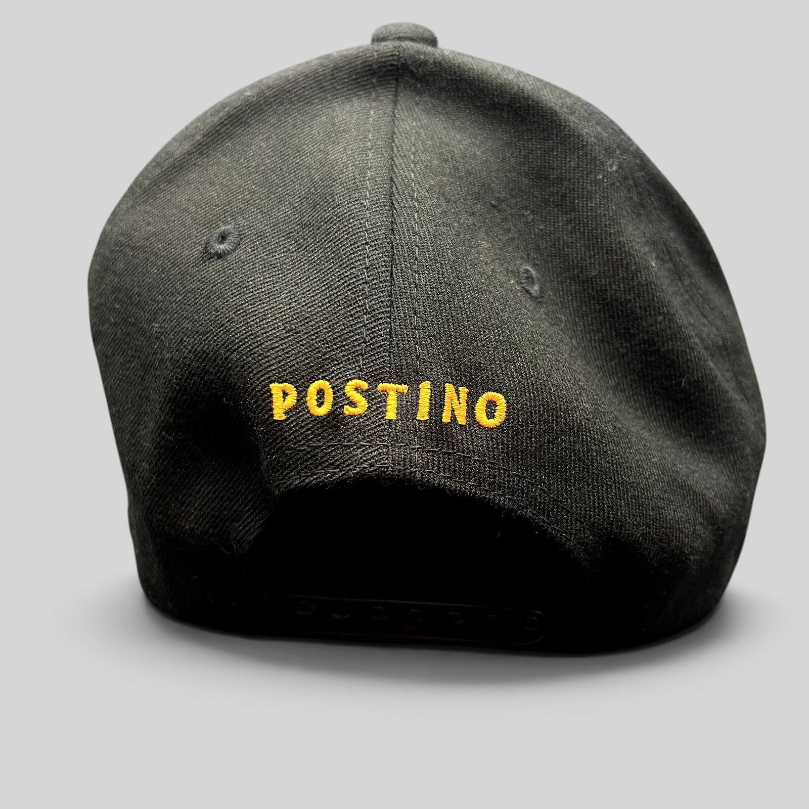 Raree Finds black snapback hat with yellow POSTINO embroidery on the back, featuring a structured Yupoong 110 design.