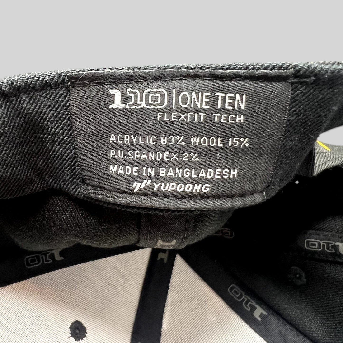 Raree Finds Postino hat interior label showing Yupoong 110 Flexfit Tech branding and material composition details.
