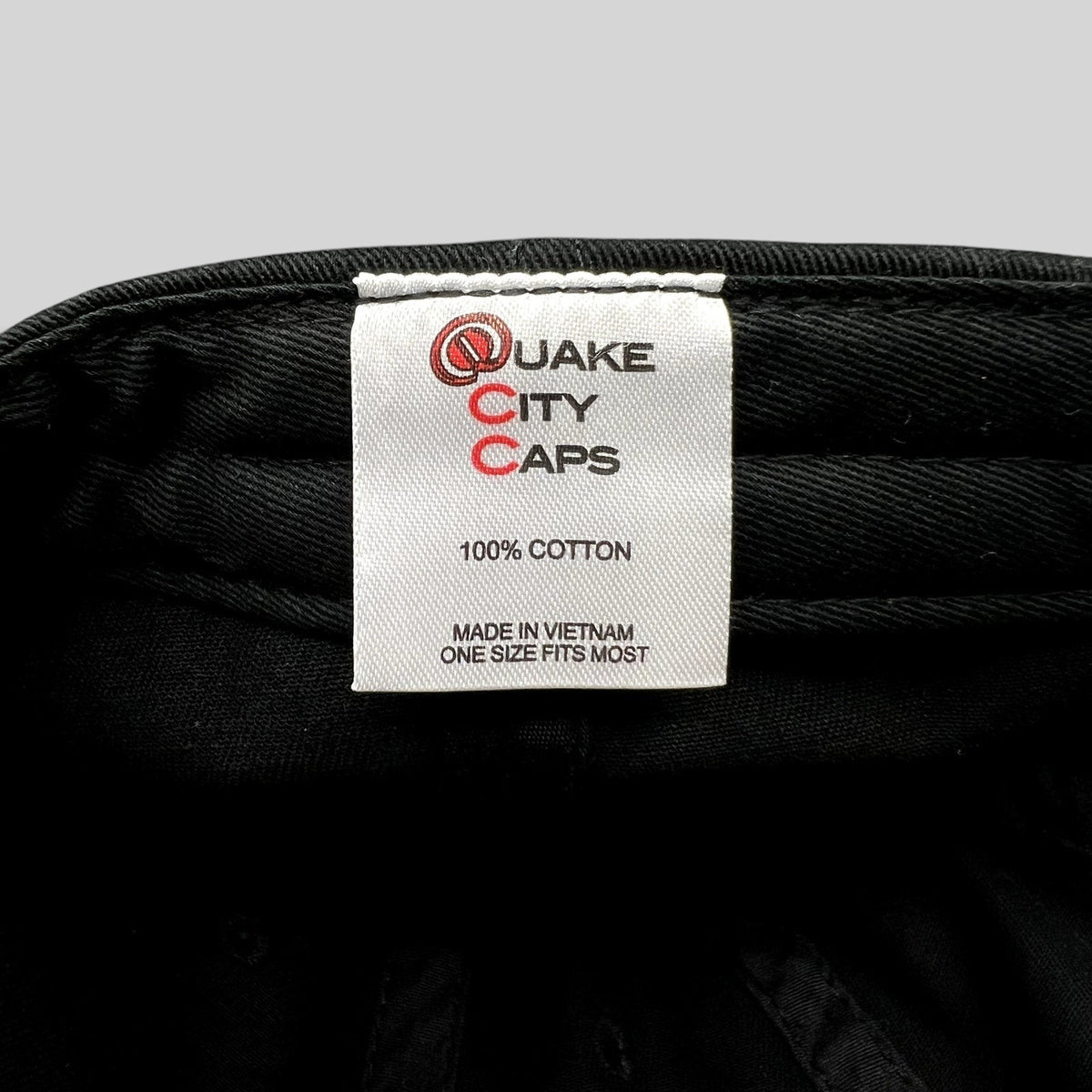 Raree Finds black cotton hat interior label showing Quake City Caps branding and 100 percent cotton material details