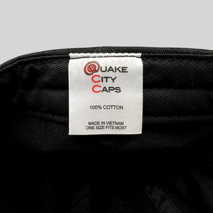 Raree Finds black cotton hat interior label showing Quake City Caps branding and 100 percent cotton material details