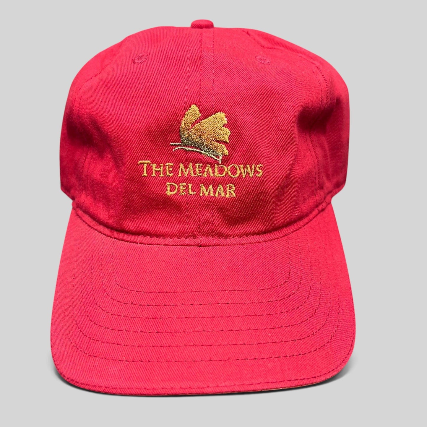 Raree Finds red cotton twill golf cap featuring The Meadows Del Mar embroidered logo and golden flower emblem.