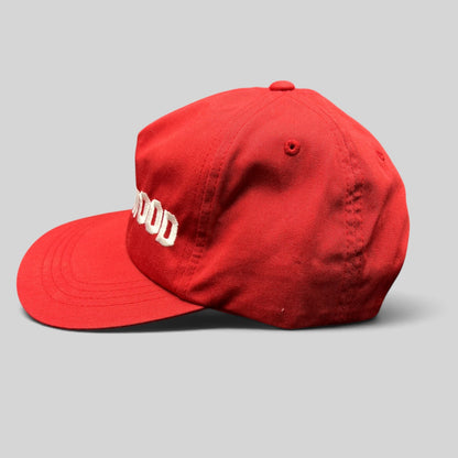 Raree Finds red Yupoong snapback hat with white HOLLYWOOD embroidery and a flat brim in a side profile view.