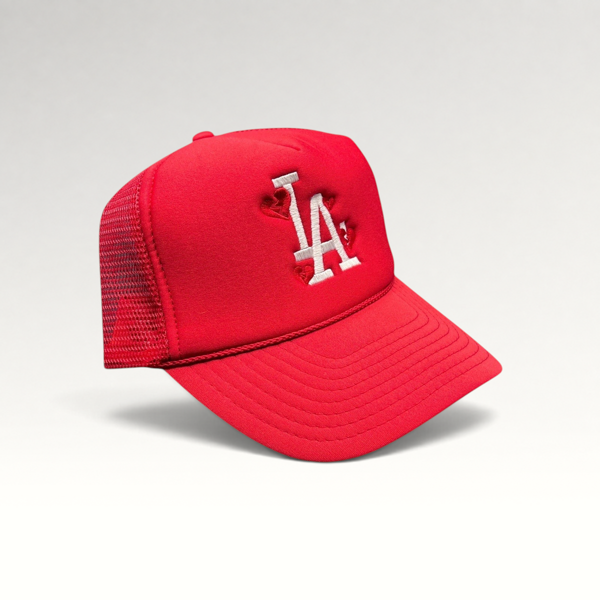 Raree Finds red Nissin Cap trucker hat with white embroidered LA logo and heart details on a foam front mesh back.
