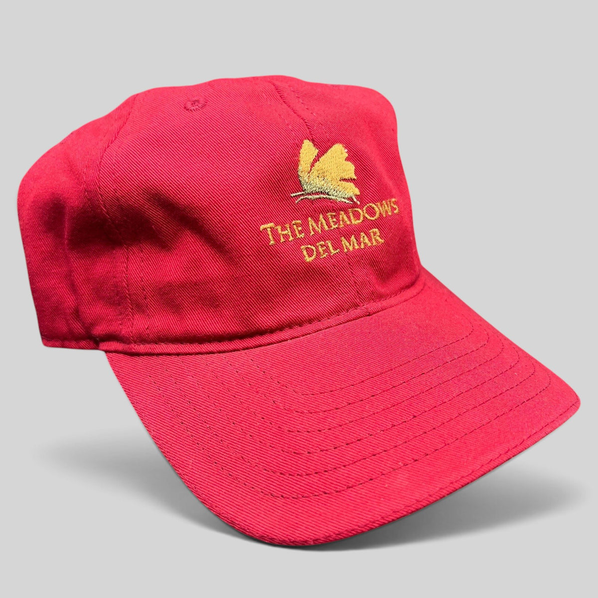 Raree Finds red cotton twill strapback golf cap featuring The Meadows Del Mar embroidered golden flower logo