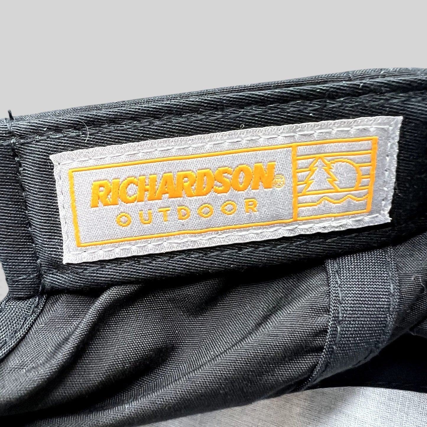 Raree Finds Richardson Outdoor label inside a black performance snapback hat with orange and grey branding